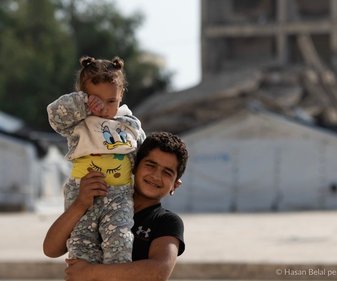 Terremoto in Siria e Turchia del 2023, un bambino tiene in braccio la sorellina con sfondo di macerie